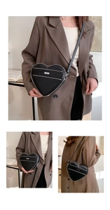 Detailed view of fashionable black heart-shaped handbag with silver zippers and leather strap