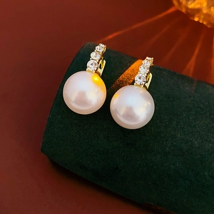 Macro detail of gold earrings with round white pearls and micro-pave crystals on velvet