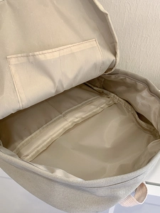 Interior view of beige canvas backpack showing large main compartment and layered pockets