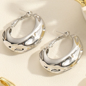 Detailed view of silver U-shaped earrings with molten liquid texture on beige paper