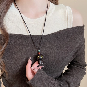 Close-up of a cute black cat pendant with green and red beads on a woven rope