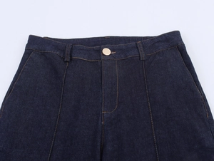 Dettaglio di jeans a vita alta blu scuro con bottoni metallici e cuciture a contrasto di denim