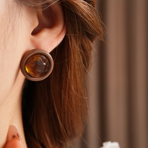 Close-up of a model wearing retro amber resin round stud earrings with a glossy finish
