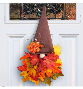 Detail of fall gnome wreath with burlap hat and autumn maple leaves on white door