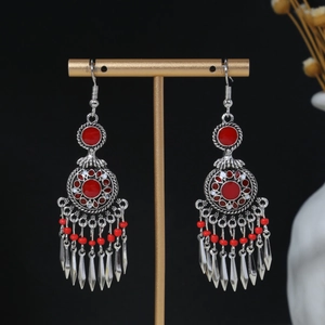 Close-up of bohemian tassel earrings with red beads on a golden display stand