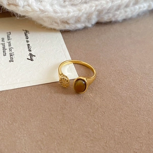Detailed close-up of golden crossover ring featuring oval tiger eye stone and small metal disc