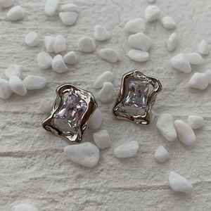 Detailed shot of silver zircon earrings with irregular molten metal edges on white stone