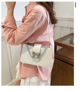 Close-up of a white shoulder bag featuring a silver chain and a metallic bow clasp