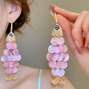 Detail of gold fish earrings with pink shell scales and blue evil eye charms