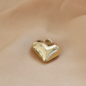 Detailed close-up of golden resin heart pendant on smooth beige silk fabric texture