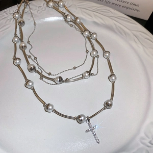 Detail shot of multilayered silver cross necklace with pearls on a ceramic tray