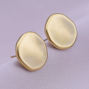 Macro view of golden irregular pebble-shaped stainless steel earrings on purple satin