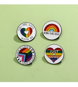 Detailed view of four rainbow enamel pins with LGBTQ+ slogans on a green background