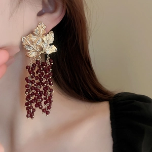 Model wearing gold leaf earrings with dark red bead tassels in a vintage drop style