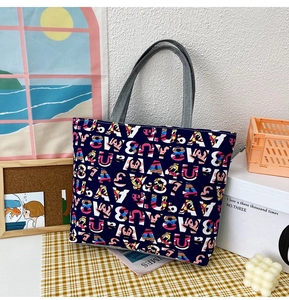 Detail of dark blue canvas tote bag featuring colorful printed letters and grey straps