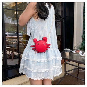 Mini red crab coin purse featuring golden chain strap worn by a model in a cafe setting