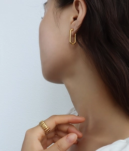 Primo piano di modella con orecchini a U e anello con trama in finitura oro 18 carati