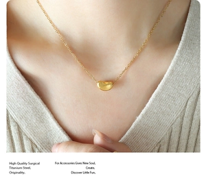 Detailed close-up of a gold bean pendant necklace on a model wearing beige knitwear