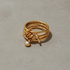 Detail of a layered gold titanium ring featuring a dangling white round cubic zirconia stone