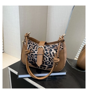 Detail of leopard print shoulder bag with brown patchwork and gold buckle on a book