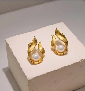 Detailed shot of golden leaf-shaped earrings with white pearls on a stone display stand