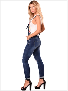 Detail of blue distressed slim fit denim overalls with knee rips and rolled cuffs