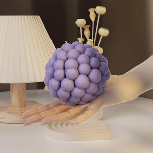 Purple textured ball-shaped aromatherapy candle with a wick held in hand for home decor