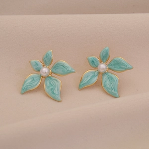 Elegant teal flower stud earrings with gold edges and pearl centers on beige fabric