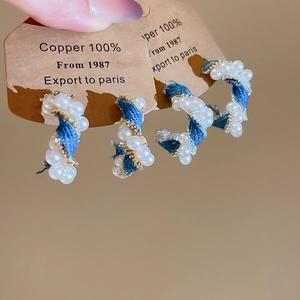Detailed close-up of C-shaped blue denim twist earrings with white faux pearls and copper base