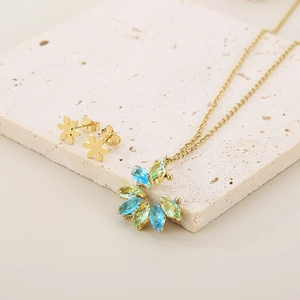 Detail of gold petal necklace and earrings set with blue and green gems on stone