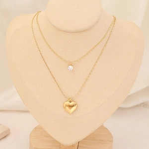 Detail of a gold double-layer necklace featuring a heart pendant and zircon stone on a bust