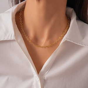 Detail view of a gold geometric ring chain necklace worn over a white shirt