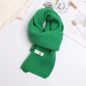 Close-up of a soft green knitted scarf with a woven label on a minimalist background