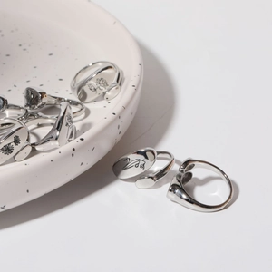 Detalle macro de anillos plateados ajustables con patrones florales en un tazón blanco