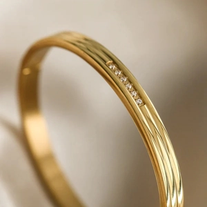 Vista macro de pulsera dorada de acero inoxidable con textura estriada y circonita
