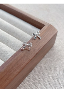 Macro shot of silver bow stud earrings on a natural wood and fabric jewelry tray