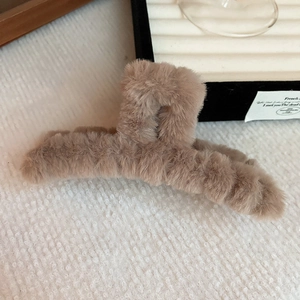 Detail of plush faux fur hair claw clip in light brown on a textured background