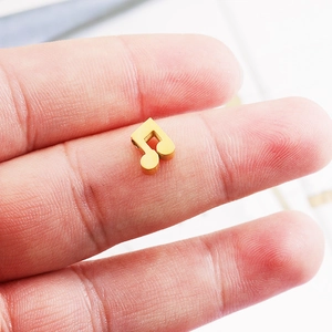 Gold music note charm bead in stainless steel held between fingers for size reference