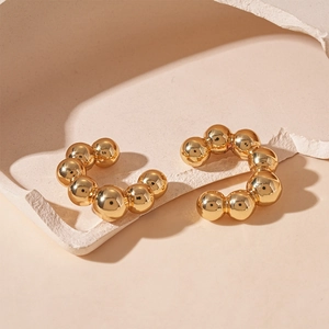 Close-up of golden geometric C-shaped ear cuffs with spherical metallic bead texture
