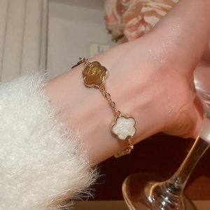 Détail d'un bracelet doré avec des fleurs ambre et blanches sur le poignet d'un mannequin