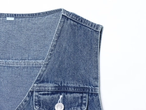 Détail du gilet en jean avec surpiqûres blanches et boutons métalliques gravés jeans