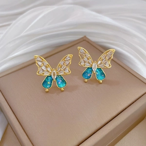 Close-up of gold butterfly earrings with blue gradient wings and sparkling crystals