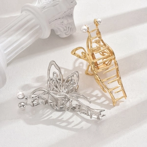 Elegant gold and silver Y2K butterfly hair claws with pearl accents on a white pillar