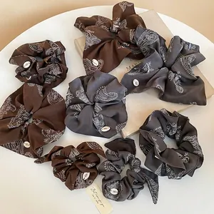 Brown and charcoal paisley print scrunchies and rabbit ear headbands on a white table