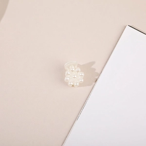 Close-up of a delicate white pearl flower hair claw clip on a soft cream background
