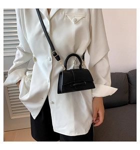 Close-up of a black hourglass crossbody bag with gold hardware on a white blazer outfit