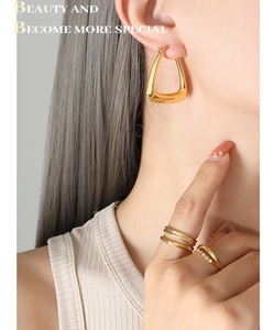 Close-up of geometric triangular gold earrings and layered rings on a female model