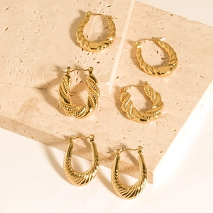 Macro view of three pairs of chunky twisted gold earrings on a stone display stand