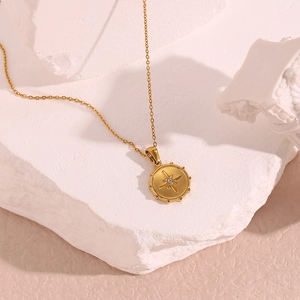 Macro detail of gold coin pendant with starburst motif and crystal on white stone