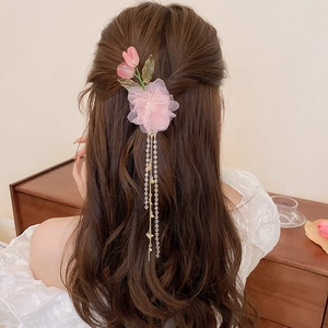 Detail of pink mesh flower hair clip with green glass leaves and golden fringe tassels